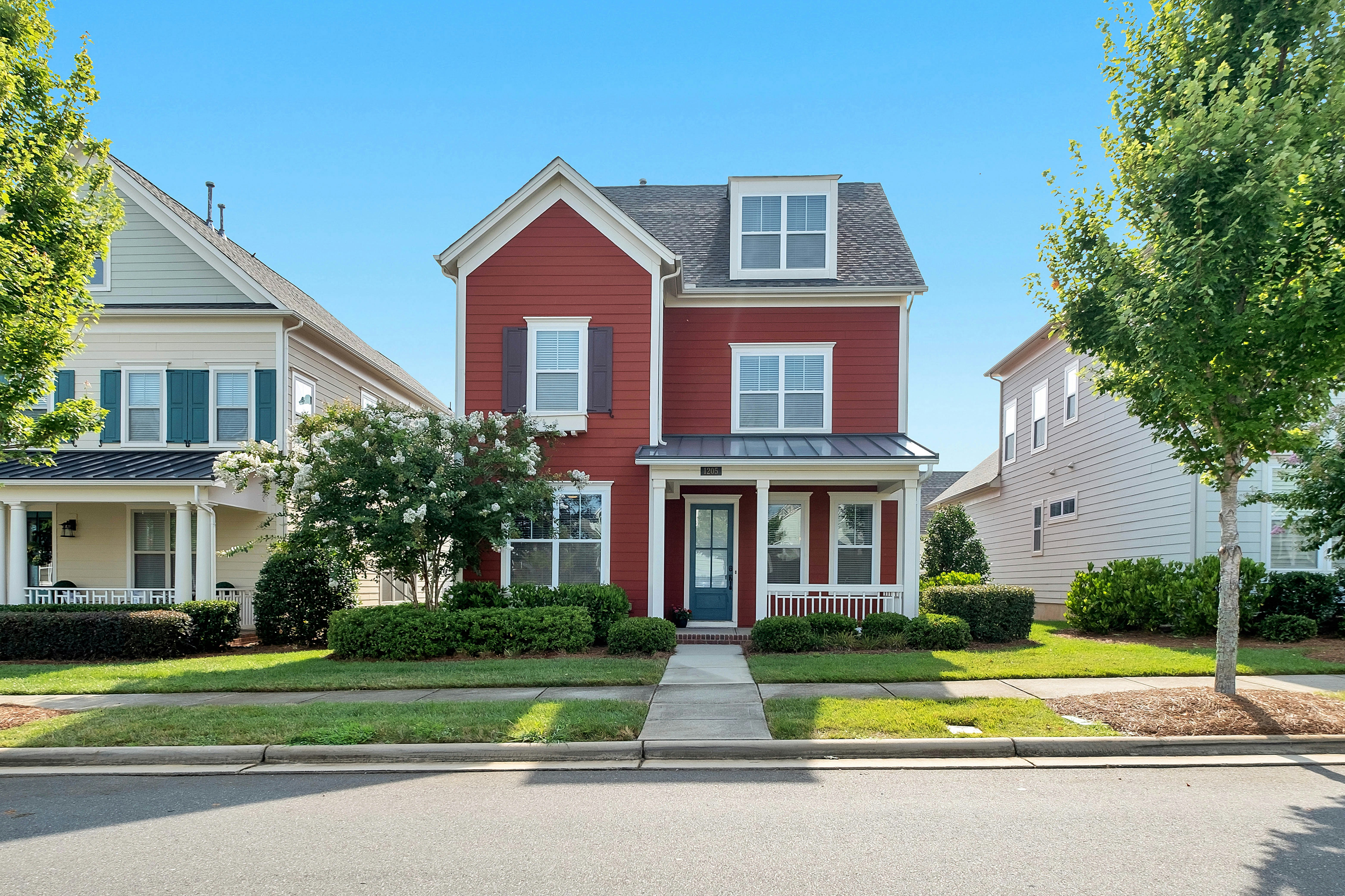 A red three-story craftsman home on a sunny suburban street